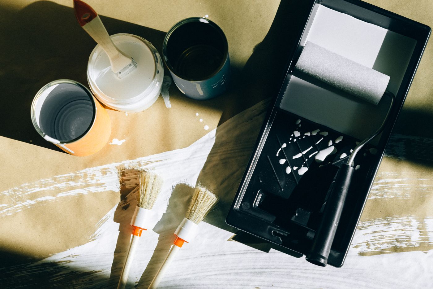 Brushes, a roller tray and open paint tins laid out on kraft paper